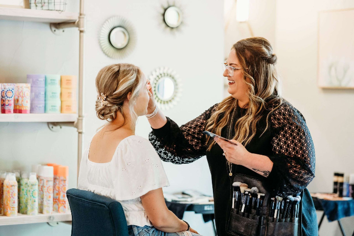 Makeup artist applying finishing touches to a bride’s makeup in the studio at Bright Luxe Salon &amp; Studio.
