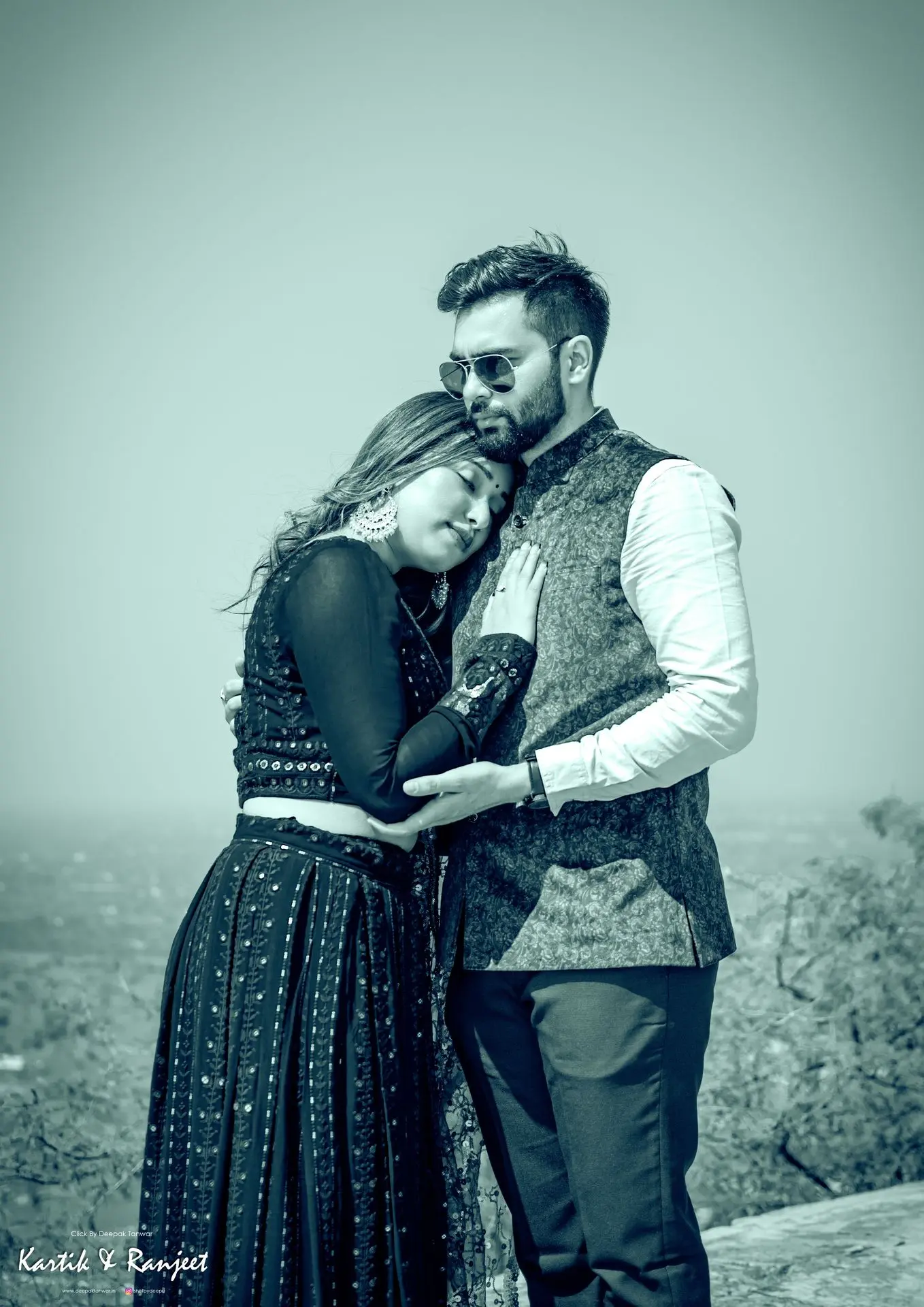 Wide shot of a couple in bright luxe turquoise and silver traditional wear sitting on a wall in a garden.