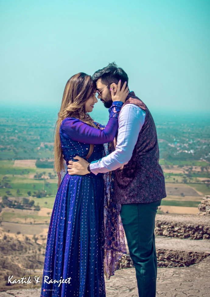 Couple in bright luxe dark blue attire standing close together with a scenic nature background.