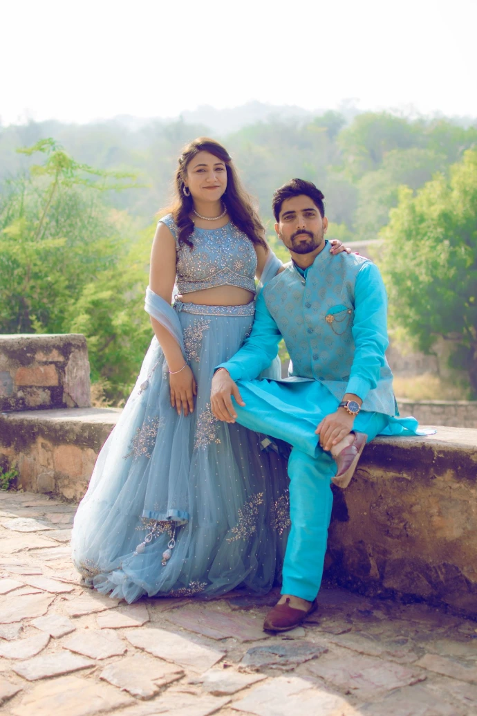 Wide shot of a couple in bright luxe turquoise and silver traditional wear sitting on a wall in a garden.